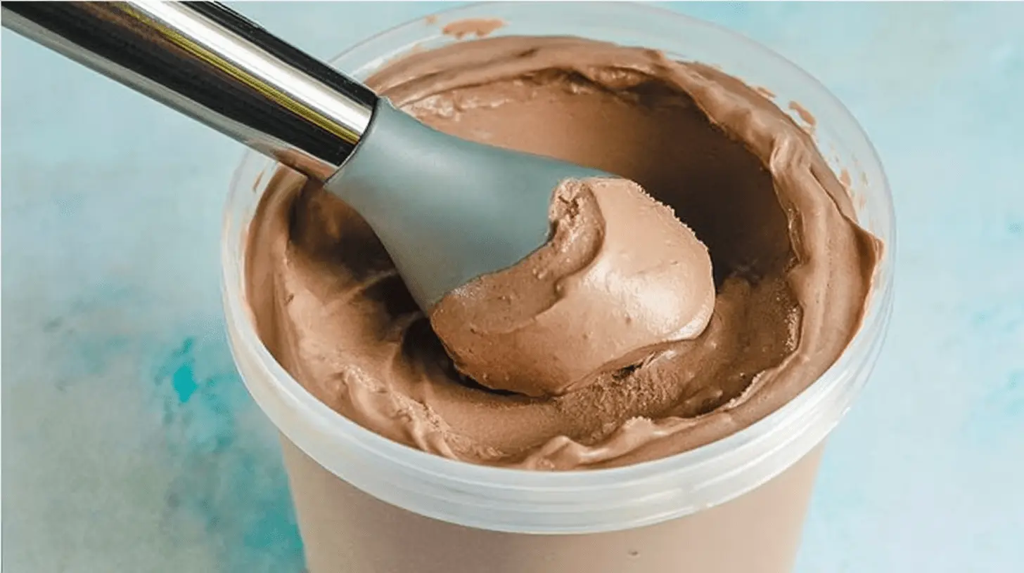 Close-up of a silver ice cream scoop serving creamy chocolate ice cream from a container, highlighting a delicious ninja creami chocolate ice cream recipe.